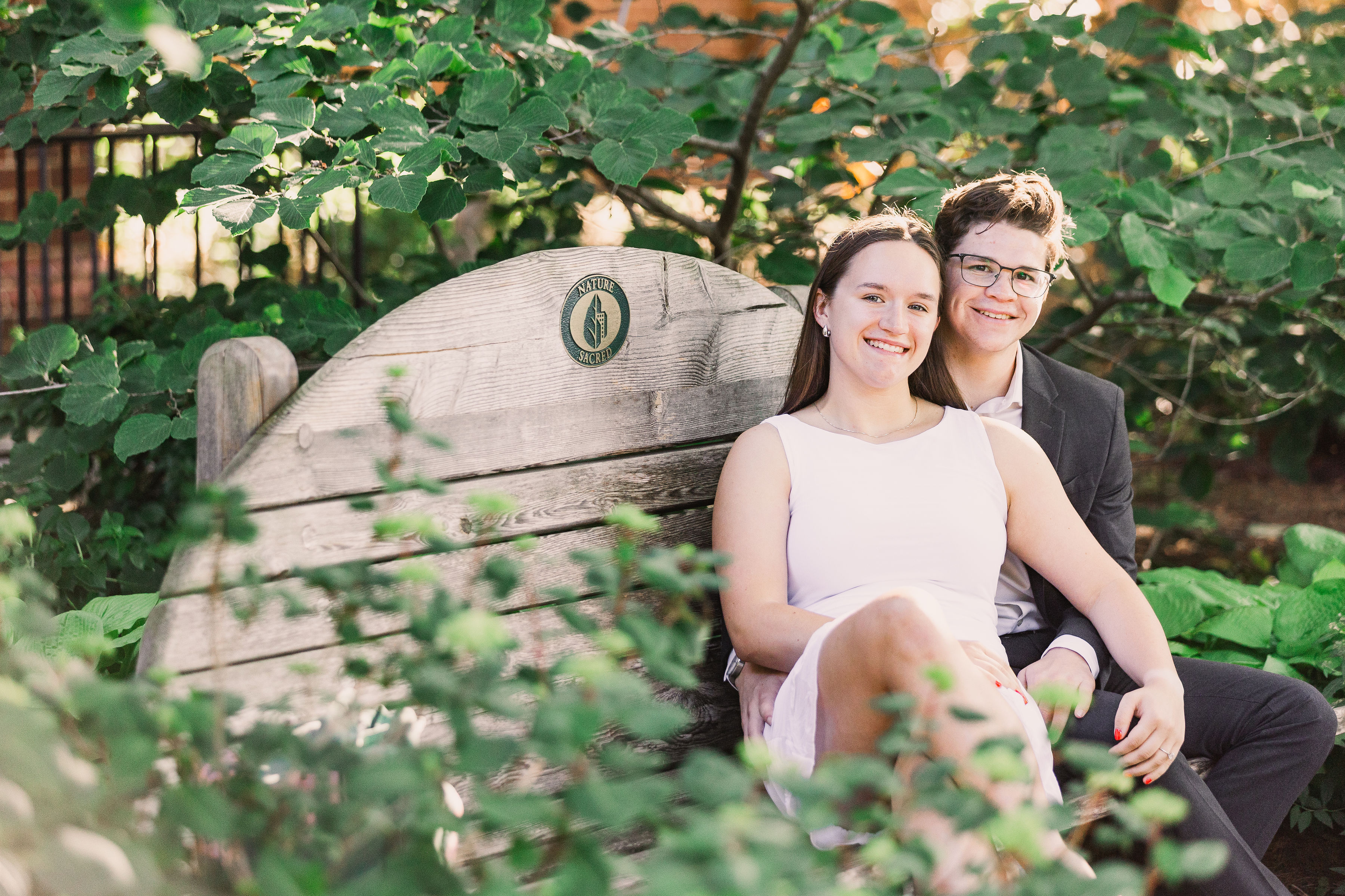 Caleb and Emma sitting together on a garden bench, surrounded by greenery